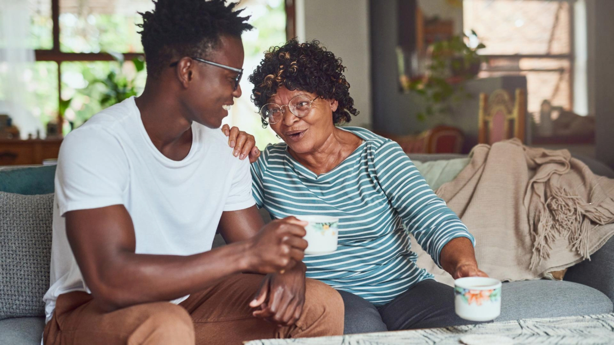 Two people are sitting close together on a couch, joyfully chatting over cups of coffee in a cozy living room setting.